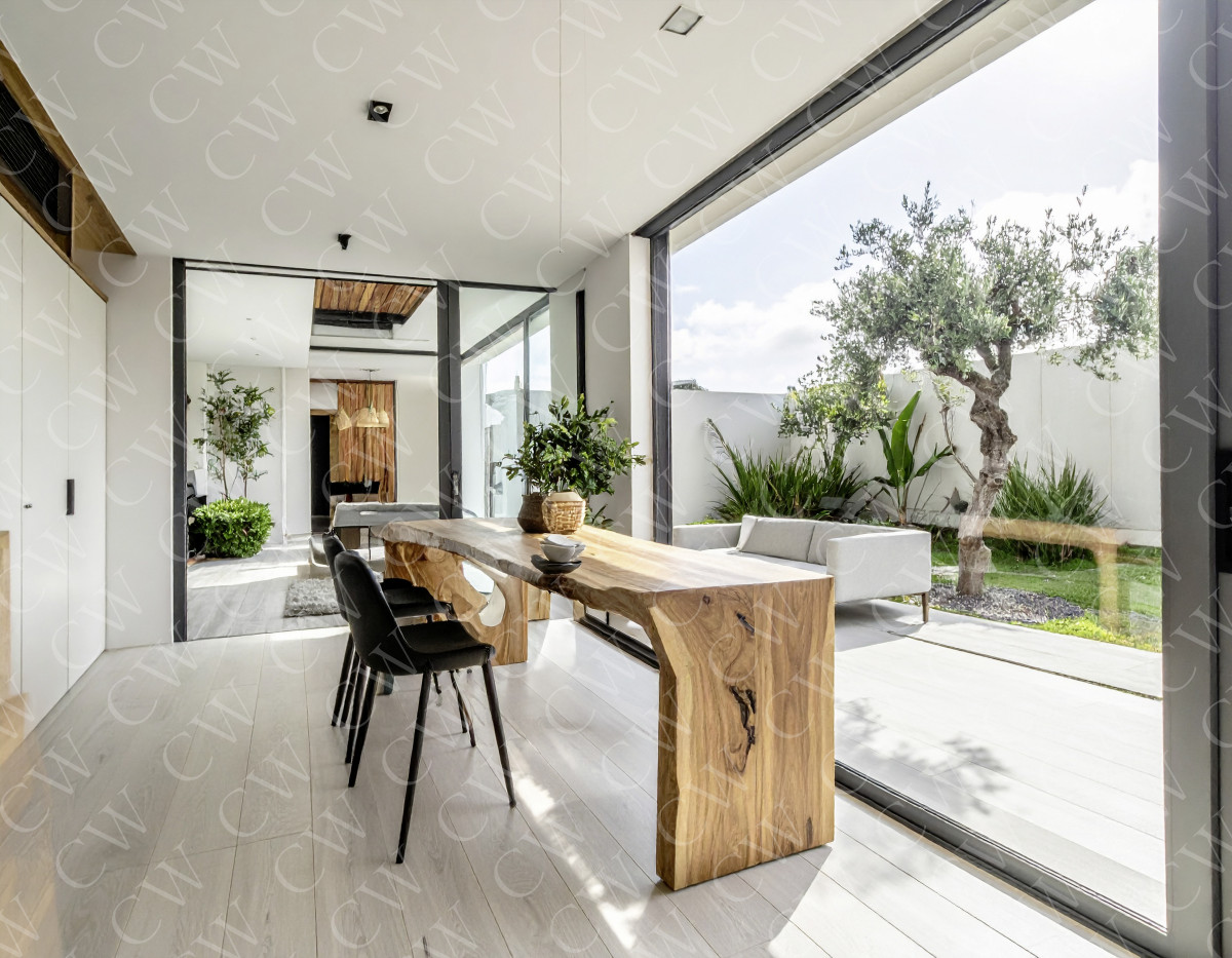 Helles Esszimmer mit Massivholztisch, schwarzen Stühlen und großen Fensterfronten mit Gartenblick.