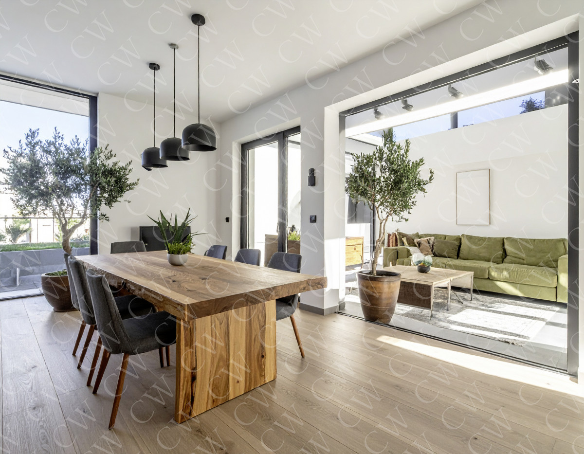 Helles Esszimmer mit massivem Holztisch, grauen Stühlen und angrenzendem Wohnzimmer mit grüner Couch.