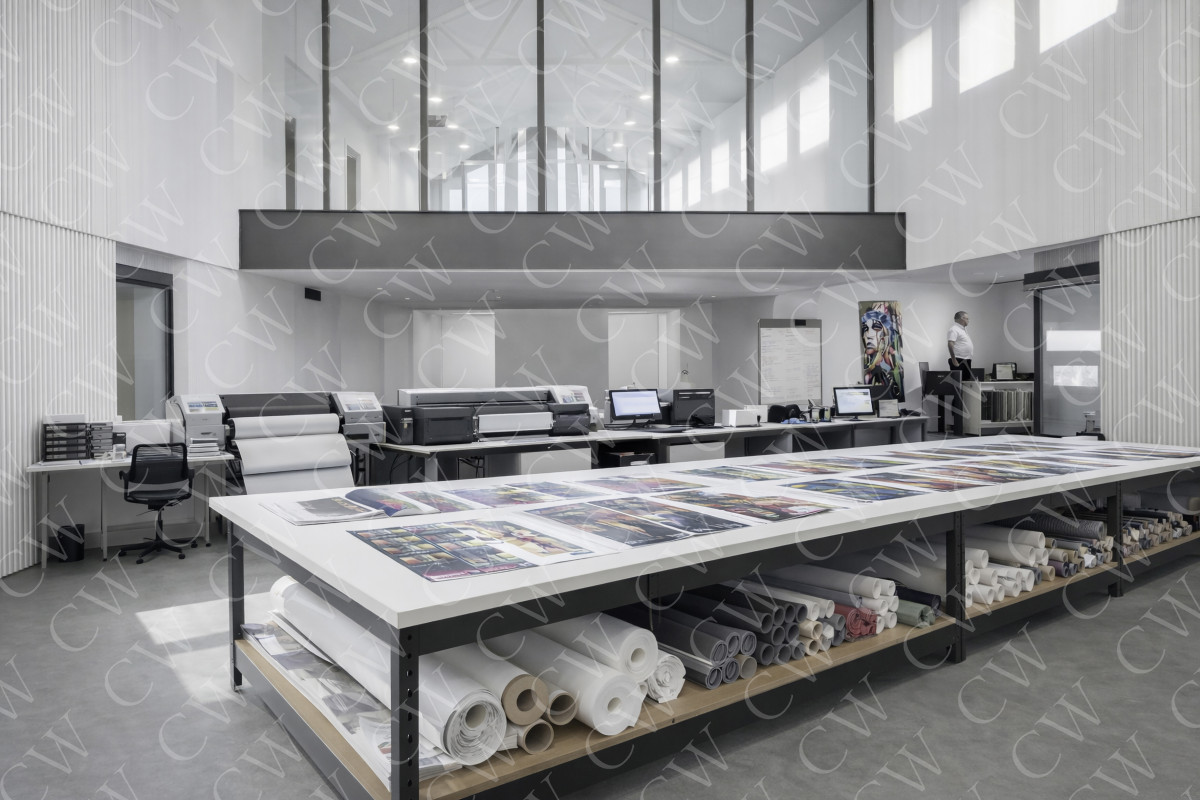 Helles Druckstudio mit großem Tisch, Plottern, Computern und ausgebreiteten Druckmustern.